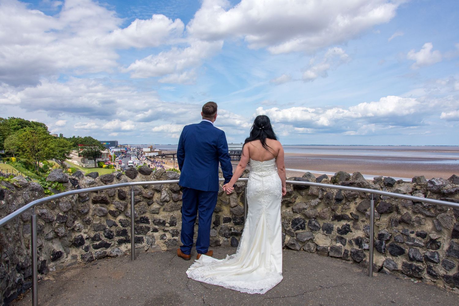 Couple in wedding attire viewing coastal scenery from stone observation deck.