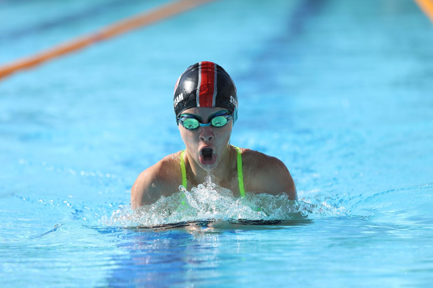 Swimmer performing breaststroke technique in bright blue pool water during competition.