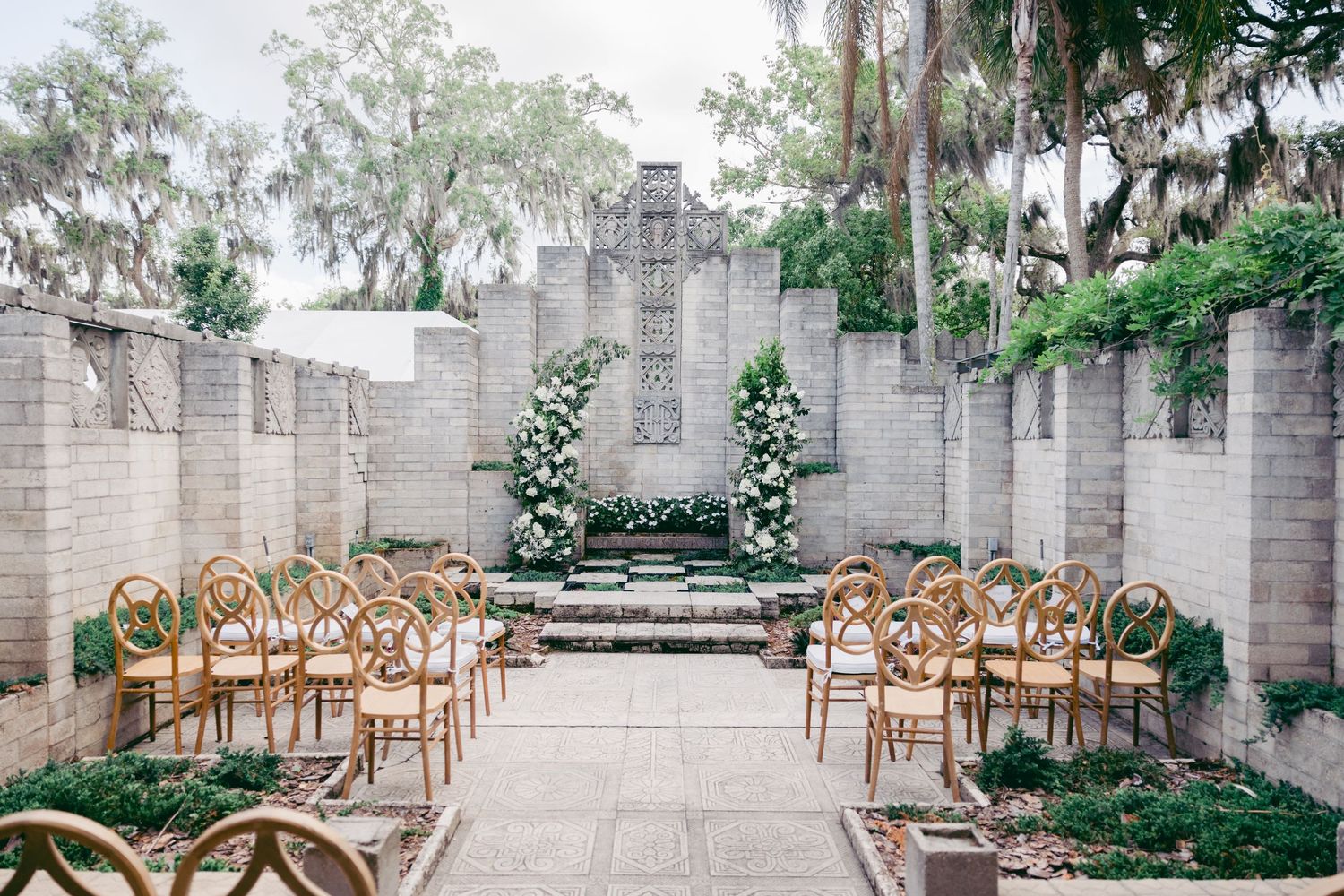 An elegant wedding venue with stone walls, floral arrangements, and gold chairs.