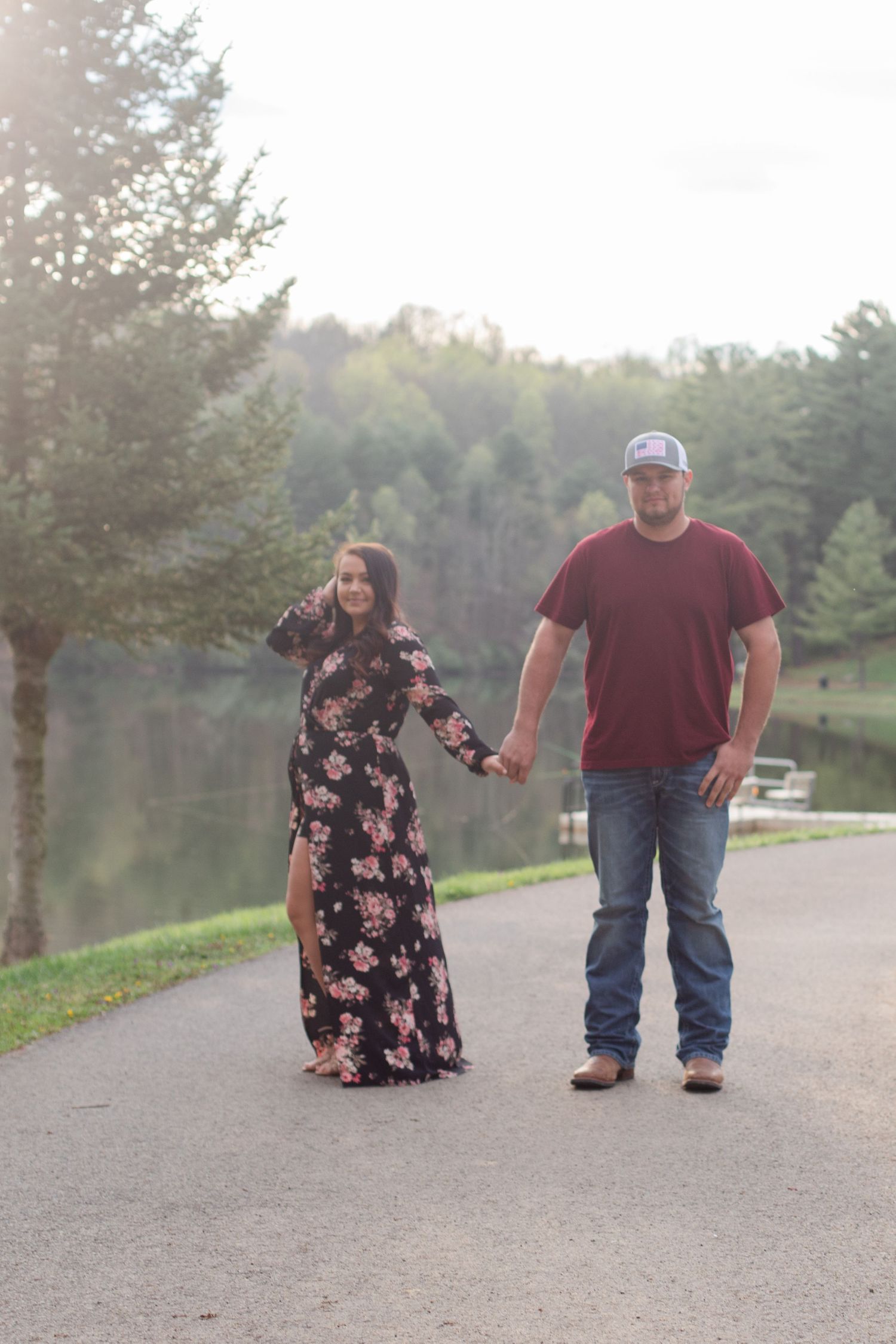 Couple walking hand in hand on a path by a lake during golden hour.