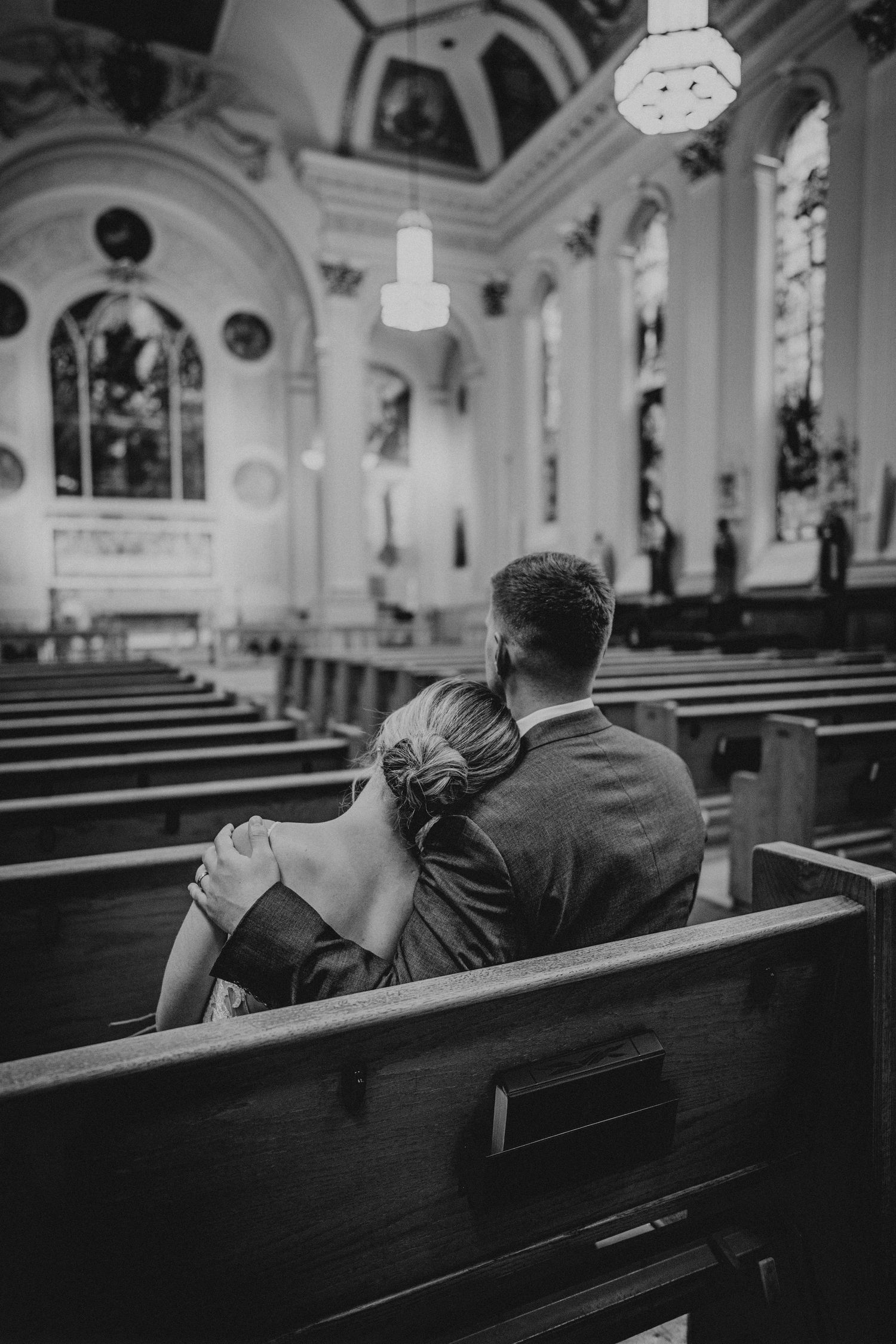 Black and white photo of a couple sharing an intimate moment in church pews.