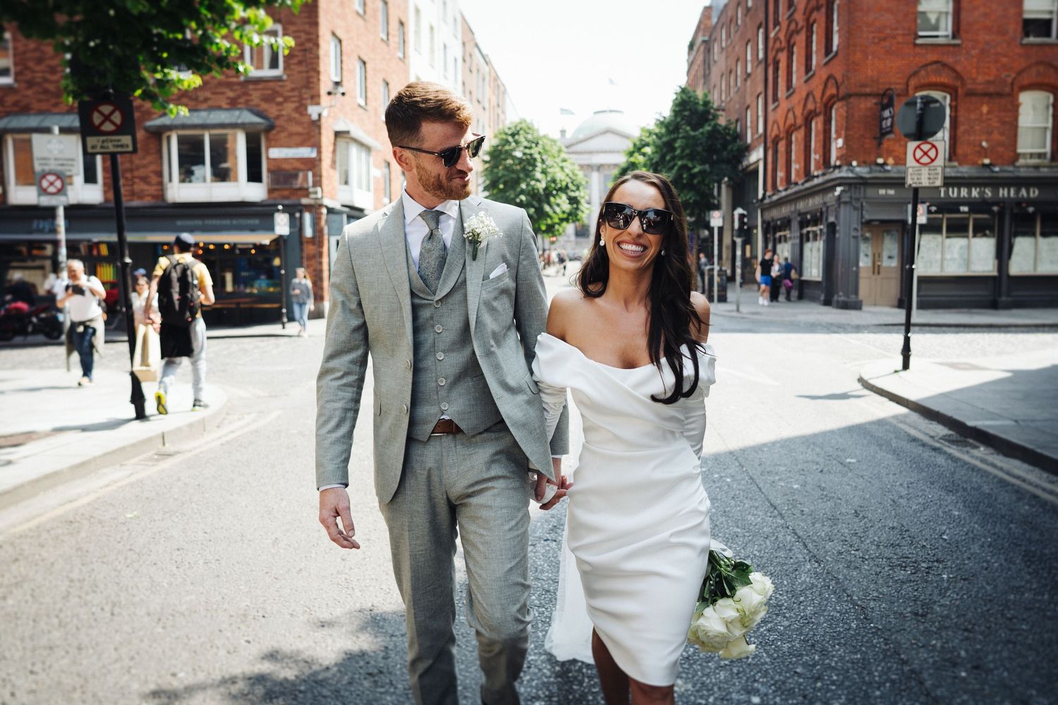 Stylish couple walking down urban street after wedding ceremony.