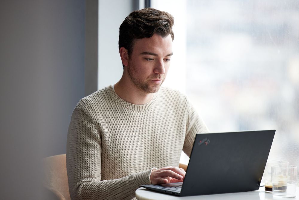 Man in a beige sweater works on a computer in the office