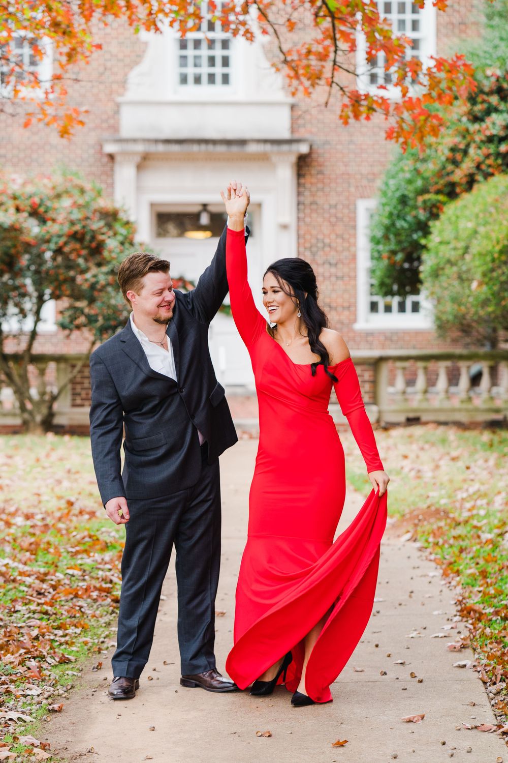 Couple in formal wear dancing joyfully on autumn path with red dress flowing.