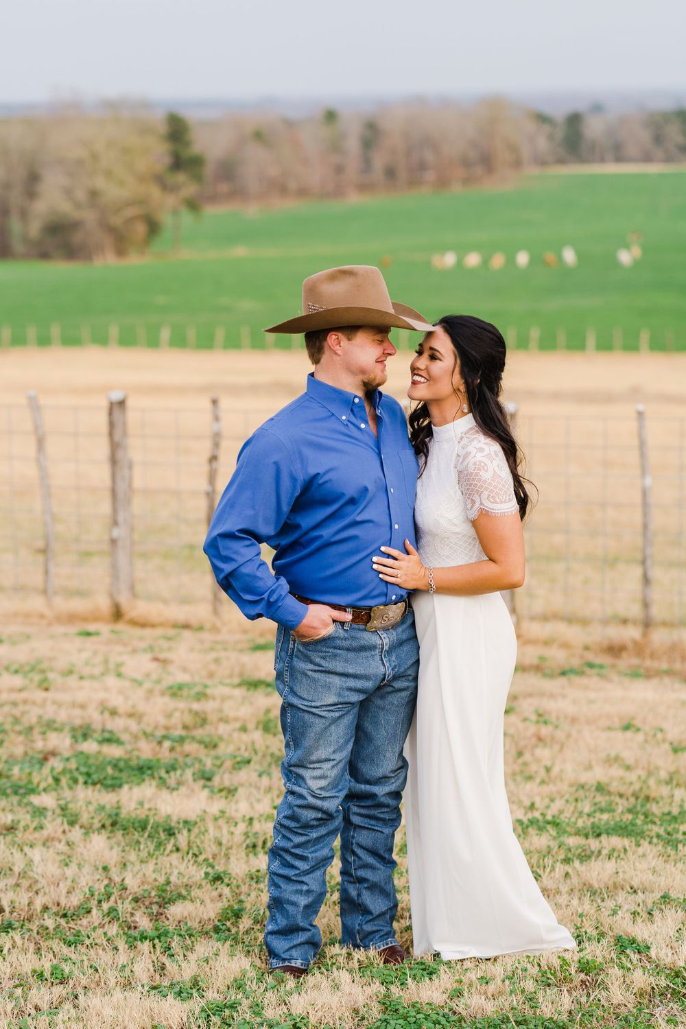 Engagement photo in rustic farm setting with couple in western attire and white dress.