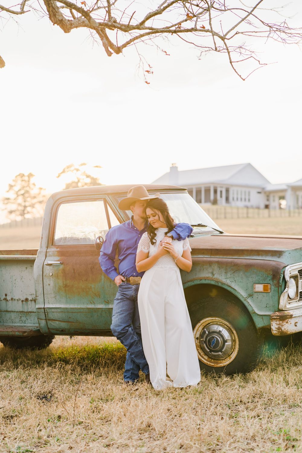 Couple poses against vintage pickup truck during golden hour sunset.