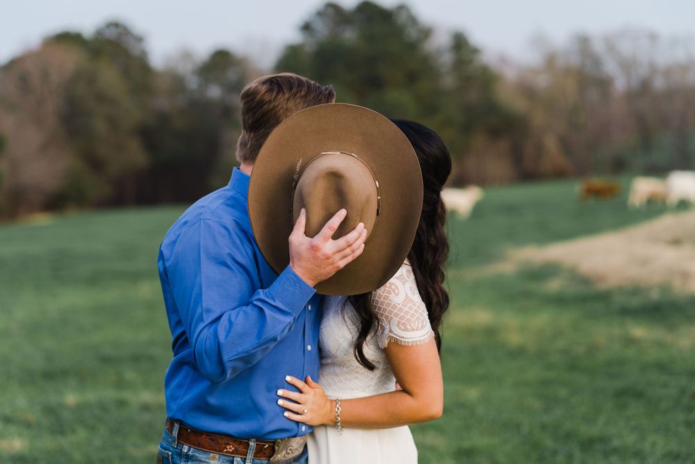 Playful moment shared between couple with cowboy hat in green field.