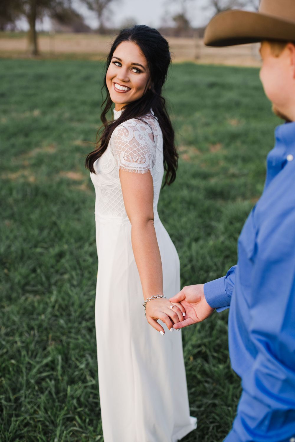 Sweet candid moment captured walking through green field in formal western attire.