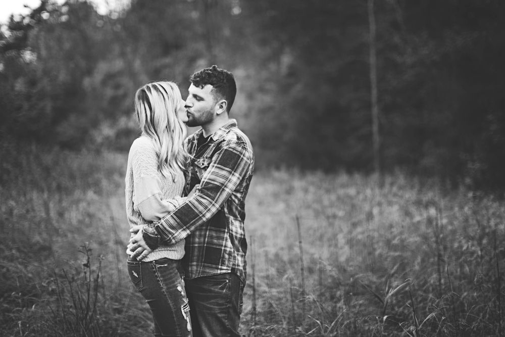 A couple embraces intimately in a black and white photo while standing in tall grass during an outdoor Fall photo session. Fall Photos