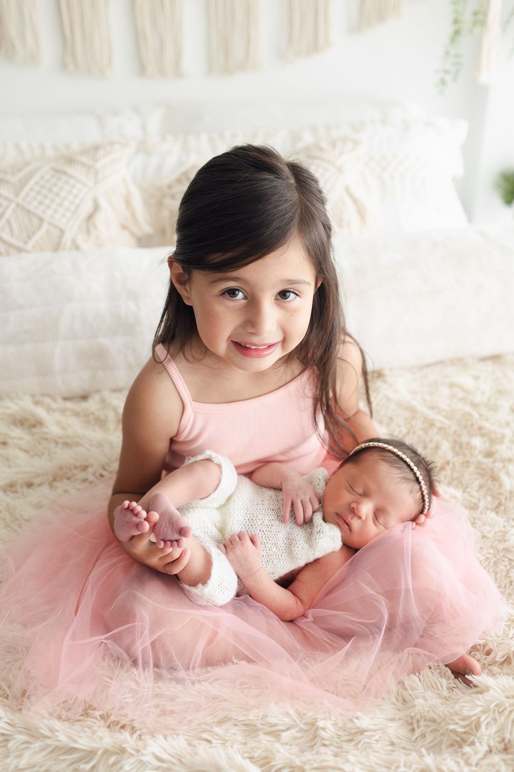 Sweet portrait on cream bedding with pink tulle dress and sleeping newborn.