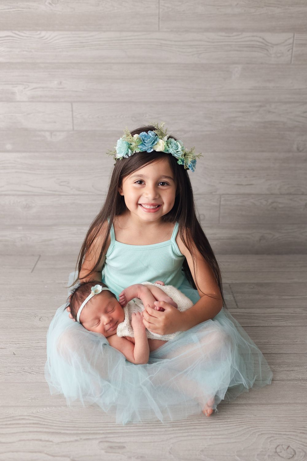 Sweet portrait with mint dress and floral crown holding sleeping newborn.