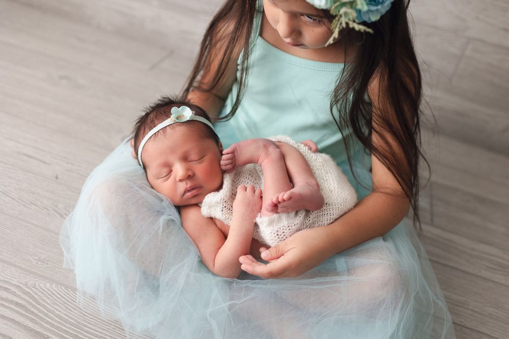 Newborn baby in white wrap being cradled in mint blue tulle dress.