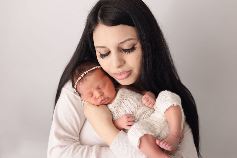 Tender moment of a newborn baby being held and cradled in soft white clothing.