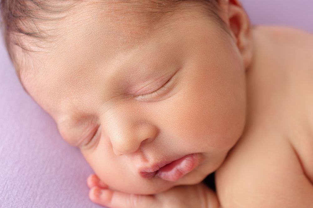 Peaceful close-up of sleeping newborn baby on purple background.