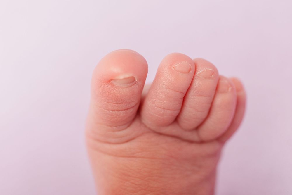 Close-up of tiny newborn baby fist against light purple background.
