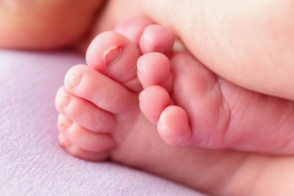 Close-up photo of tiny baby feet with delicate pink toes resting on soft pink fabric.