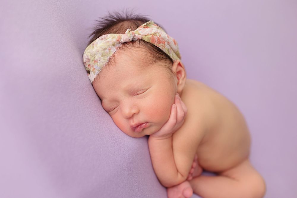 Sleeping newborn wearing a lace headband posed on purple background.