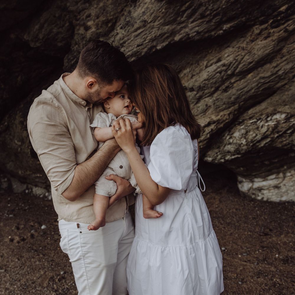 Intimate family photo in neutral clothing sharing loving moment inside rocky cave setting.