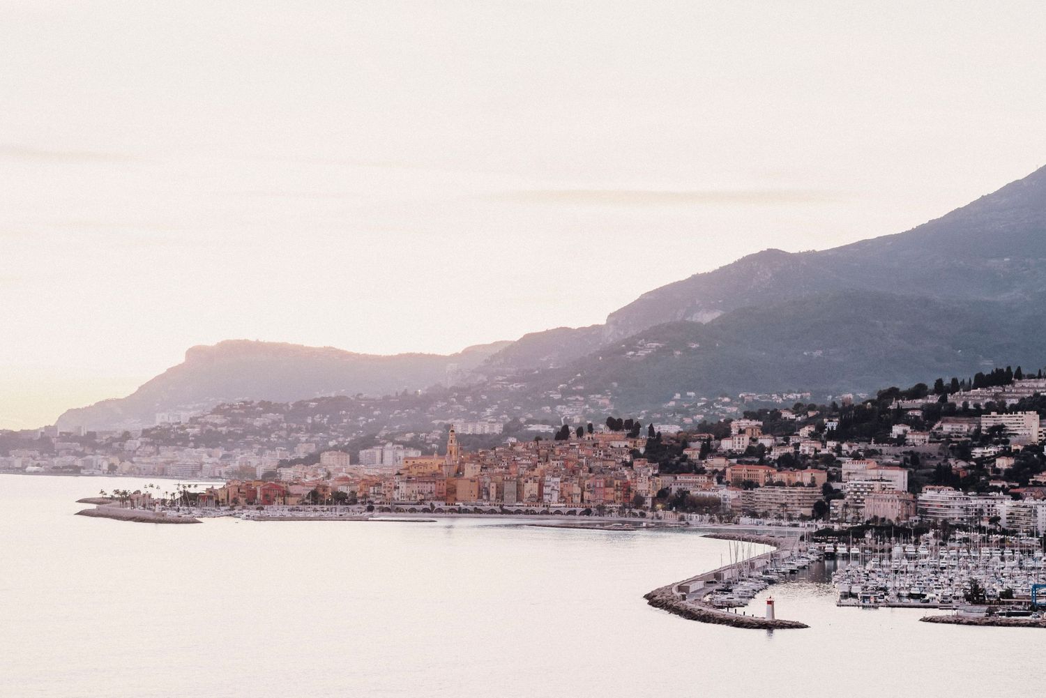 Scenic coastal Mediterranean town with mountains and harbor at sunset.