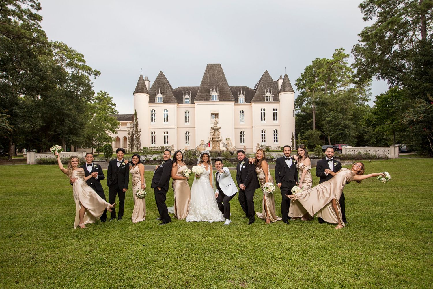 Wedding party poses on expansive lawn in front of elegant chateau-style mansion.