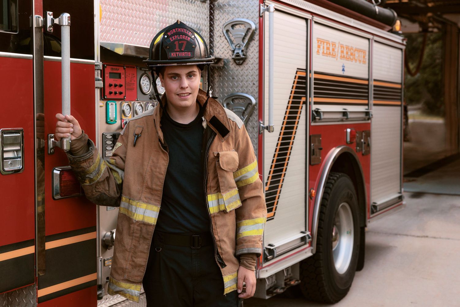 A firefighter in protective gear stands in front of their fire truck during a photo session.