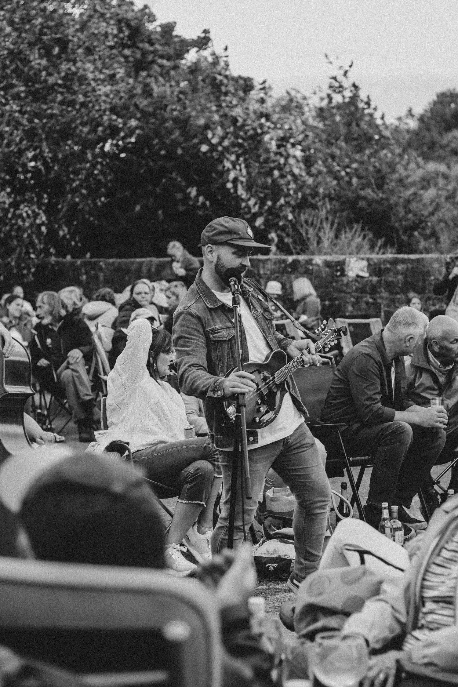 Musician performs with guitar for seated outdoor crowd at daytime event.