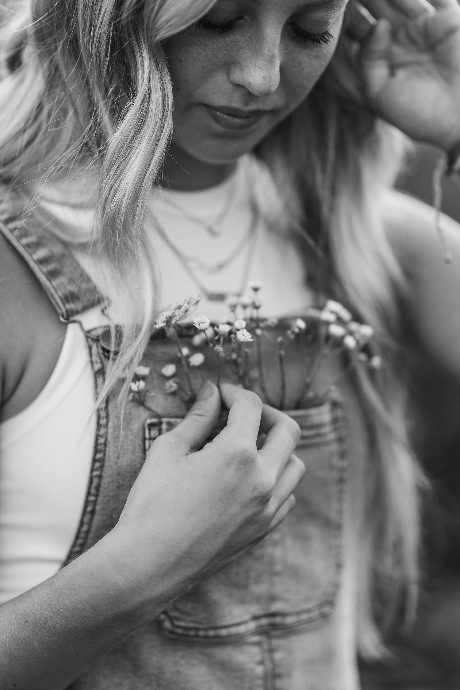 Black and white close-up of woman holding delicate wildflowers against denim overalls.
