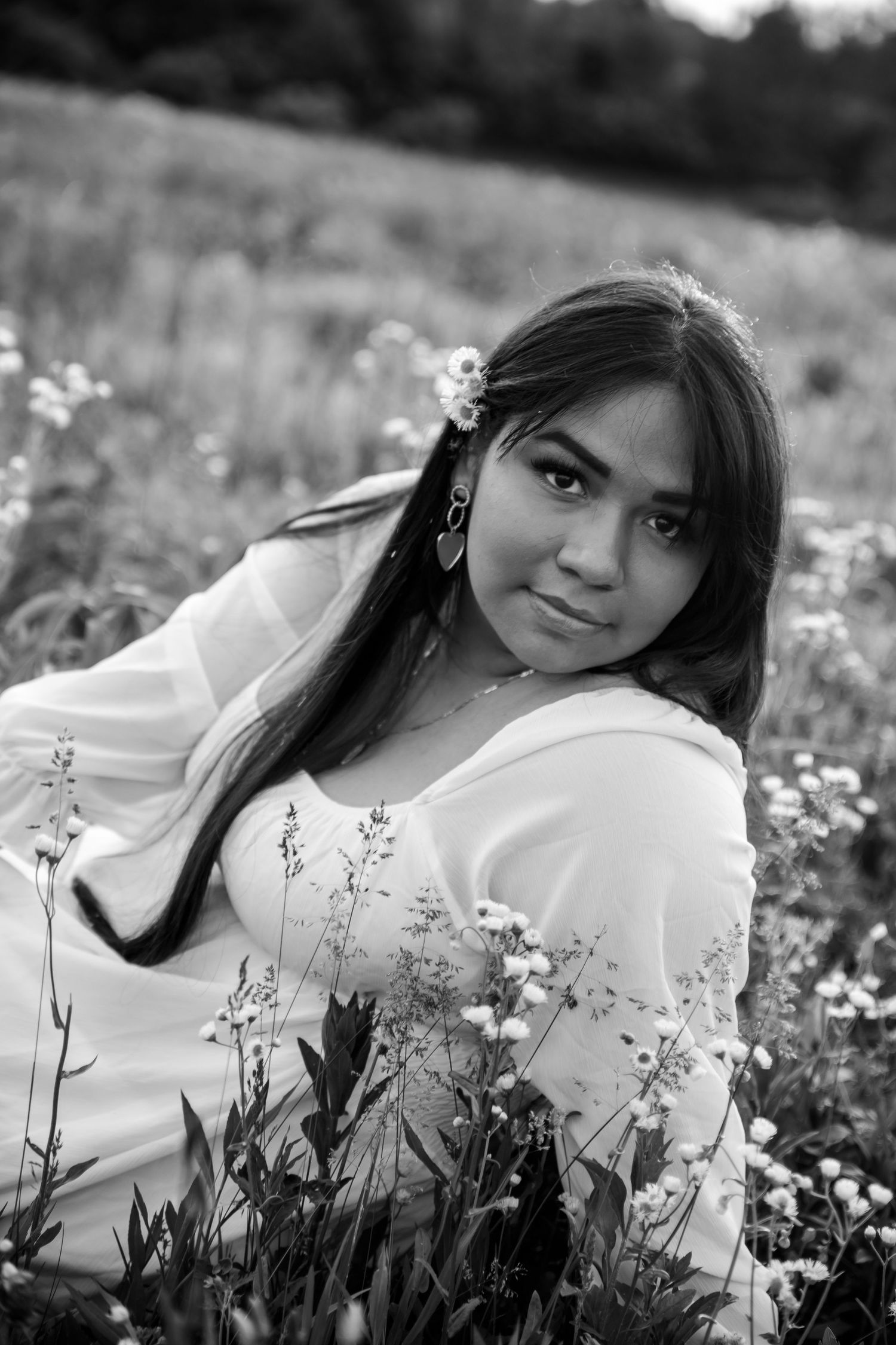 Black and white portrait of a woman in a white dress surrounded by delicate wildflowers in a meadow.