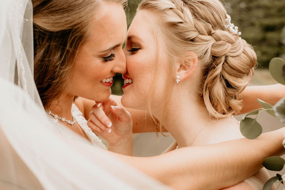 Close-up of two brides sharing an intimate moment under a flowing veil on wedding day.