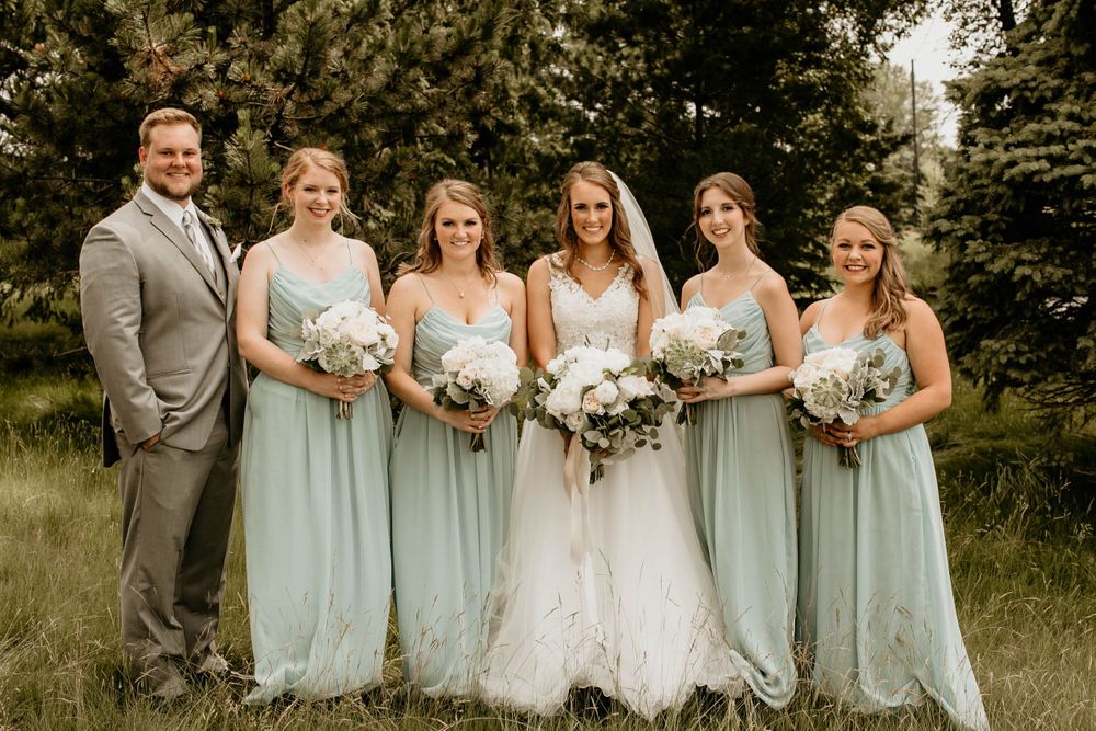 Wedding party smiling in green field with bridesmaids in mint dresses and groomsman in gray suit.