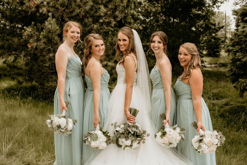 Bride wearing veil surrounded by four bridesmaids in mint green gowns holding white floral bouquets.