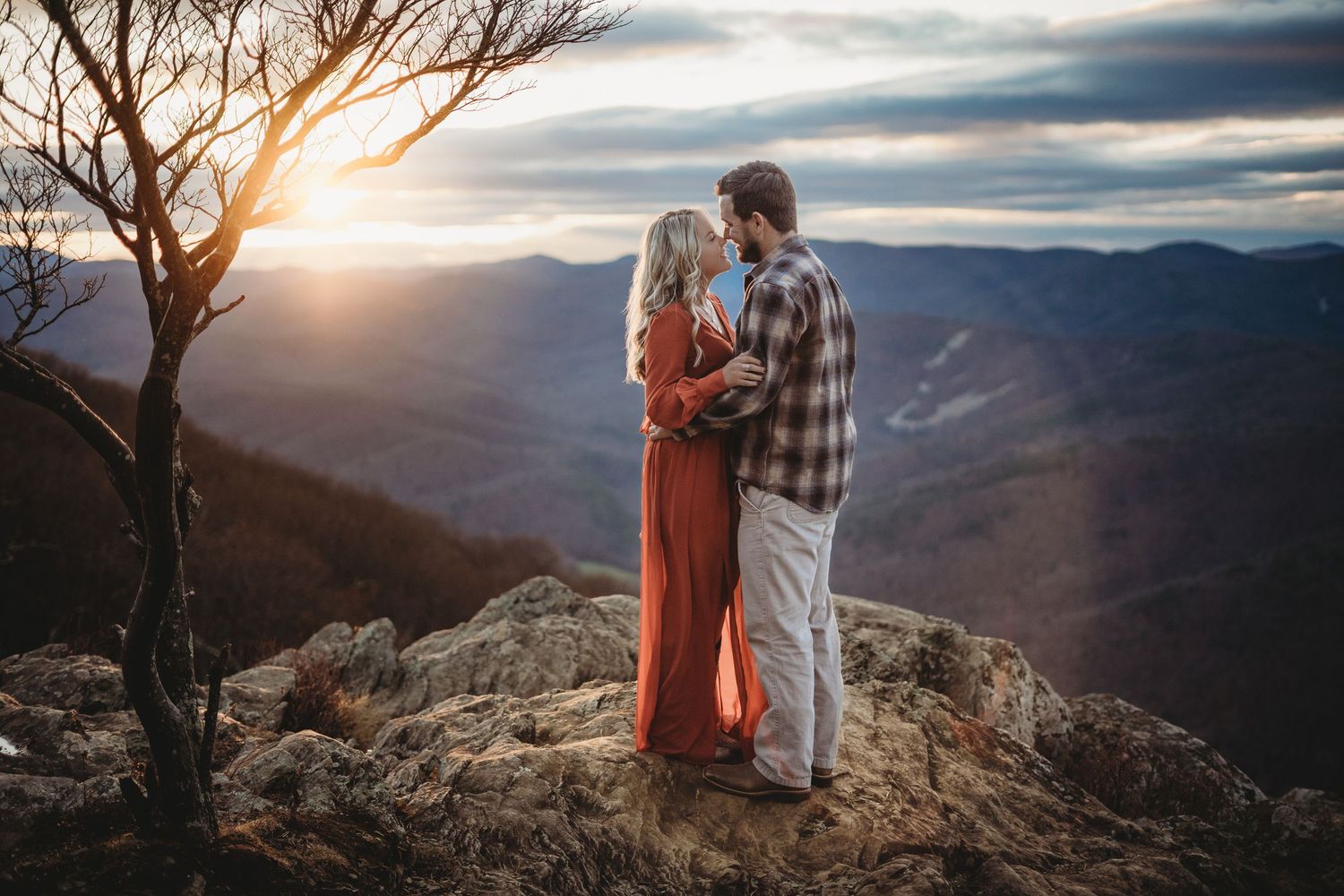 Dramatic mountain overlook during sunset with silhouetted figures against colorful sky.