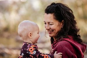 A smiling mother holds her baby outdoors, sharing a tender moment in a warm autumn setting.