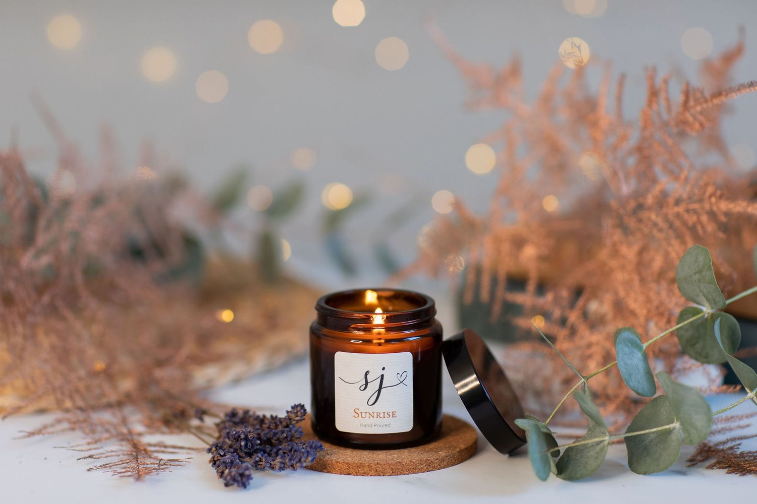Aromatic candle with dried lavender and eucalyptus leaves on white surface from a product photoshoot.