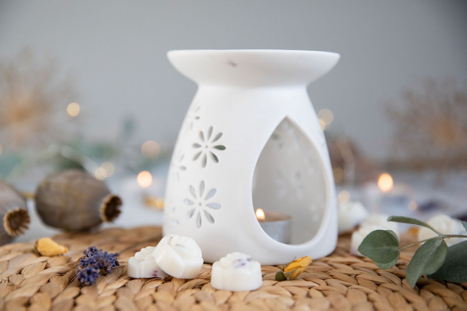White ceramic oil burner with floral cutouts and decorative stones from a product photoshoot.