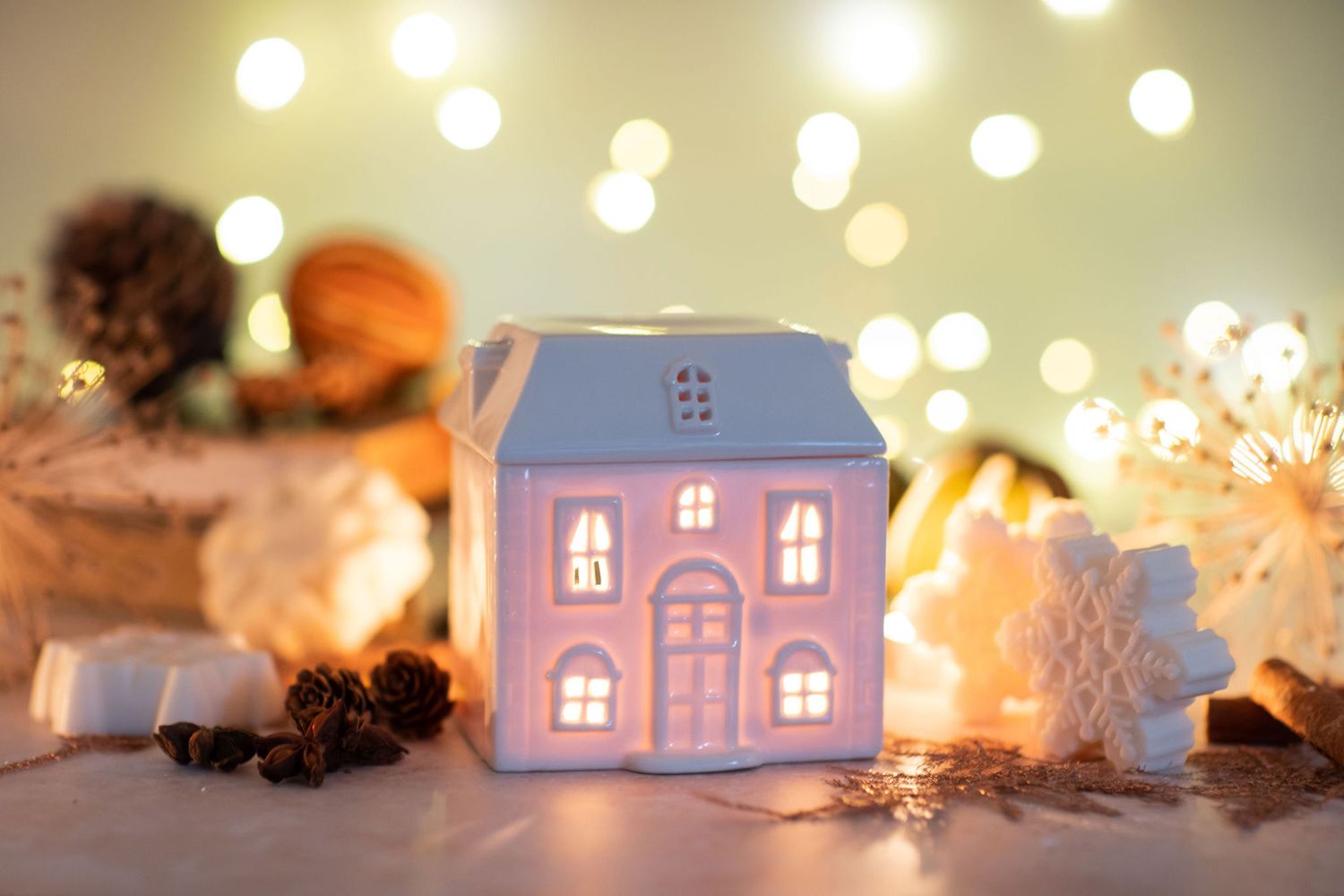 Illuminated ceramic house decoration with string lights and pine cones from a product photoshoot.