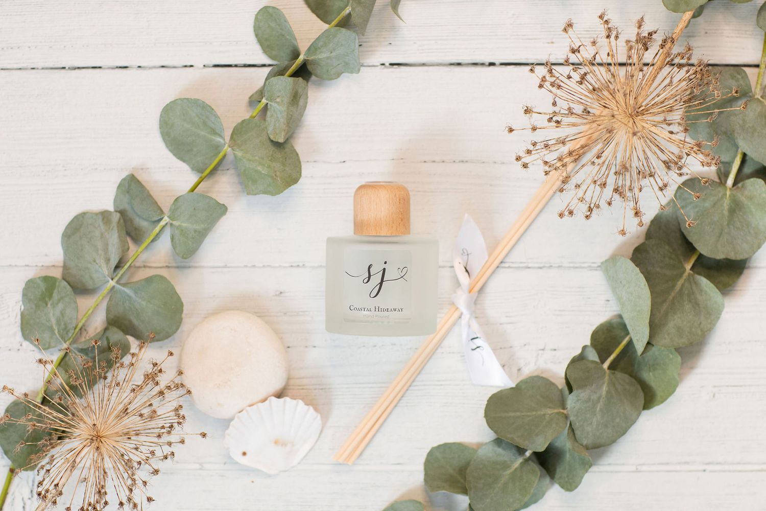 Essential oil bottle with eucalyptus leaves and dried flowers on white wooden surface from a product photoshoot.