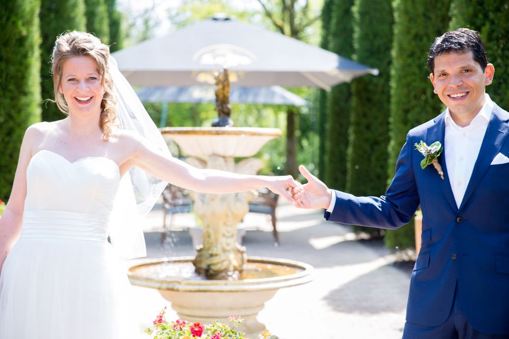 Wedding couple posing playfully by an ornate garden fountain.