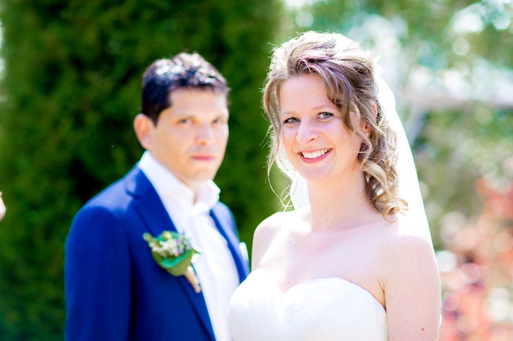 Wedding portrait with bride in focus and groom in background against garden setting.
