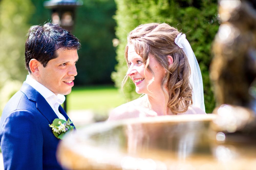 Wedding couple sharing a tender moment by an ornate fountain in a garden.