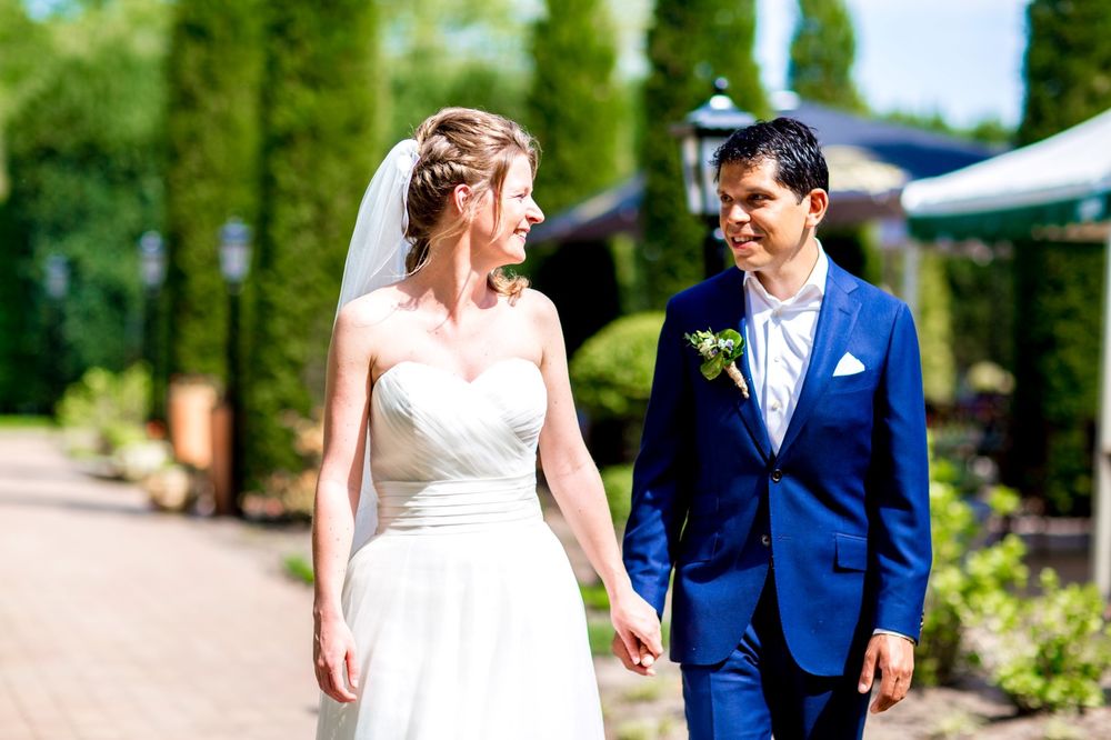 A newlywed couple walks together outdoors, with the bride in white and groom in navy blue sharing a joyful moment.