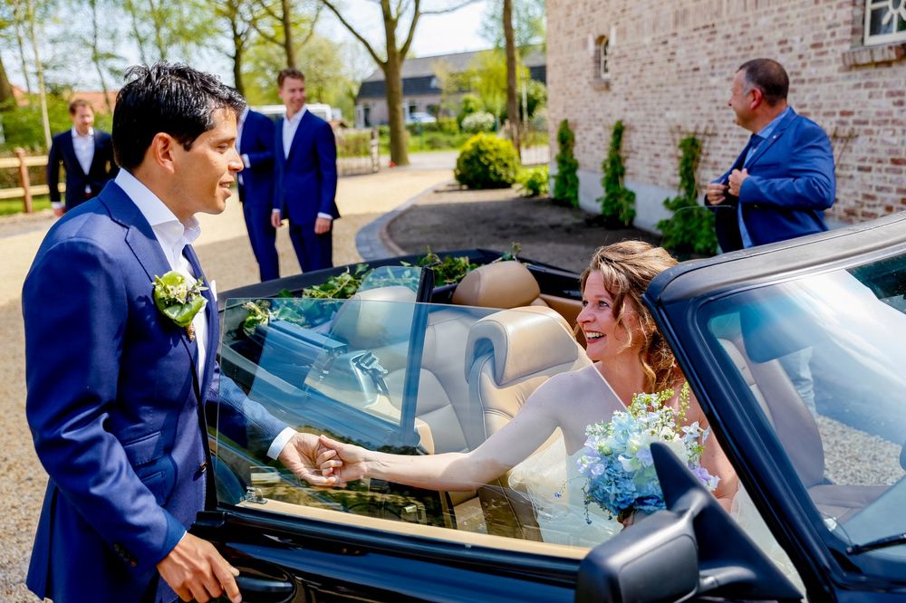 A couple interacts by a convertible car during their wedding celebration.