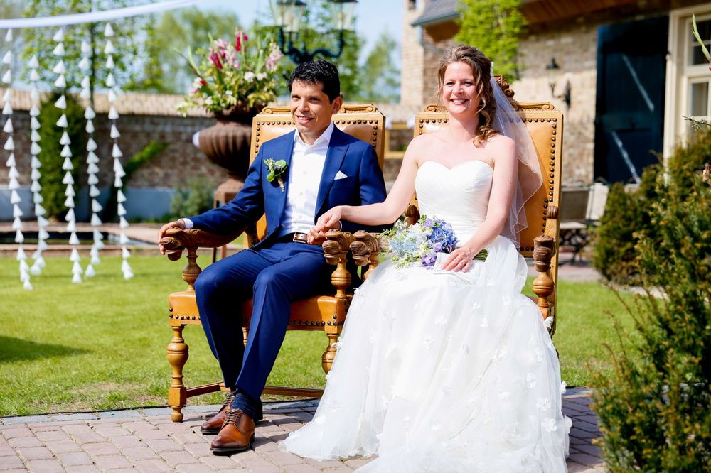 A couple sits in wooden chairs during their outdoor garden wedding ceremony.