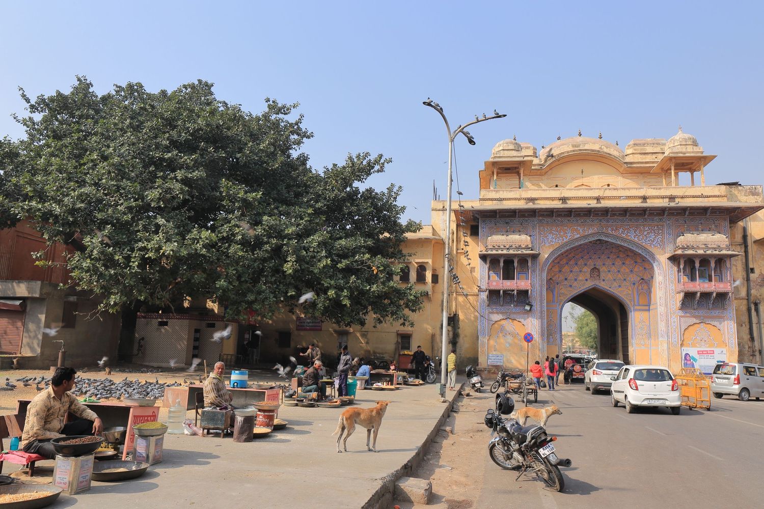 Historic city gate entrance in Jaipur with traffic and pedestrians on a sunny day.