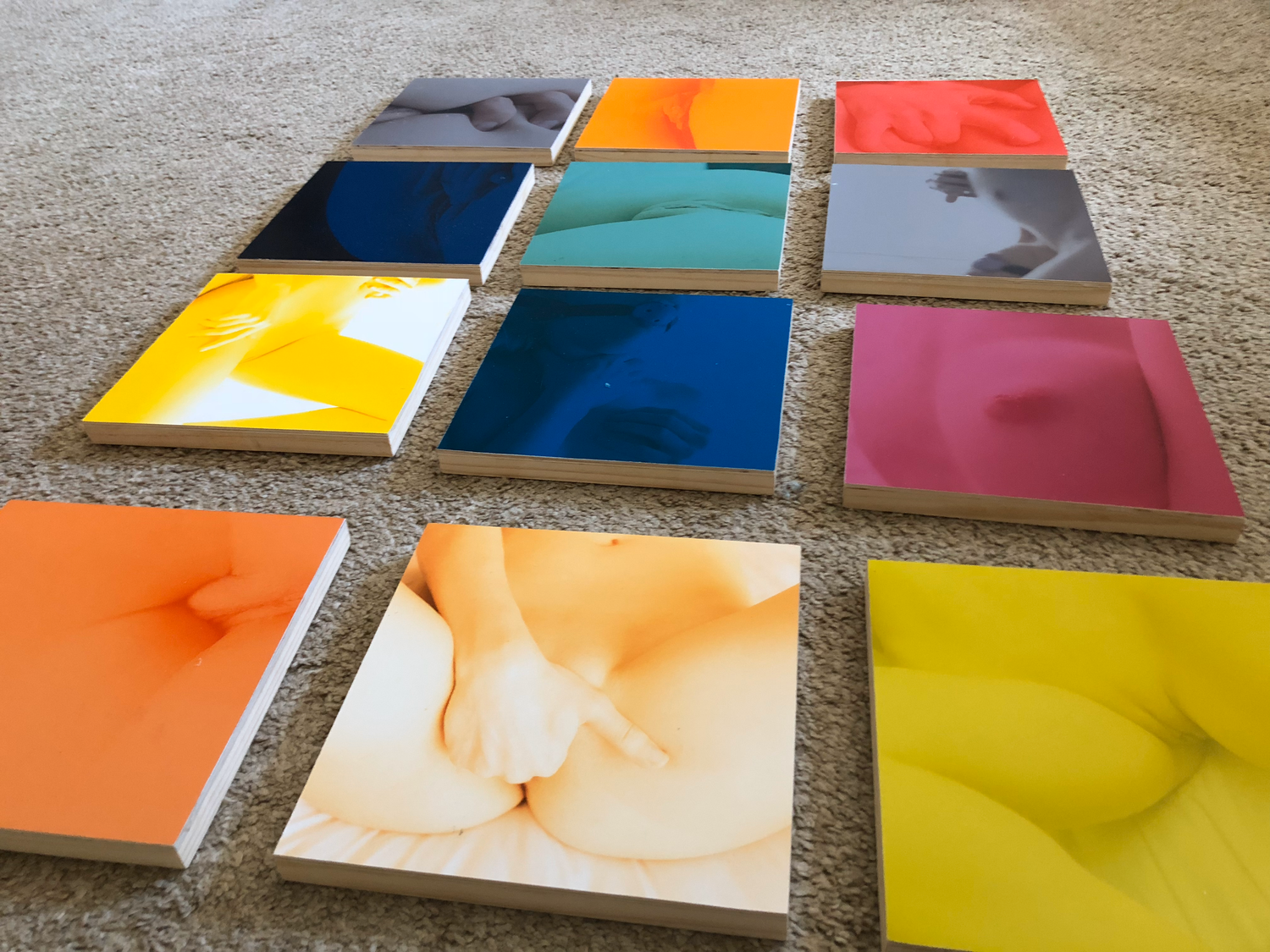 Colorful collection of glossy square art panels arranged on gray carpet showcasing vibrant hues and abstract designs.