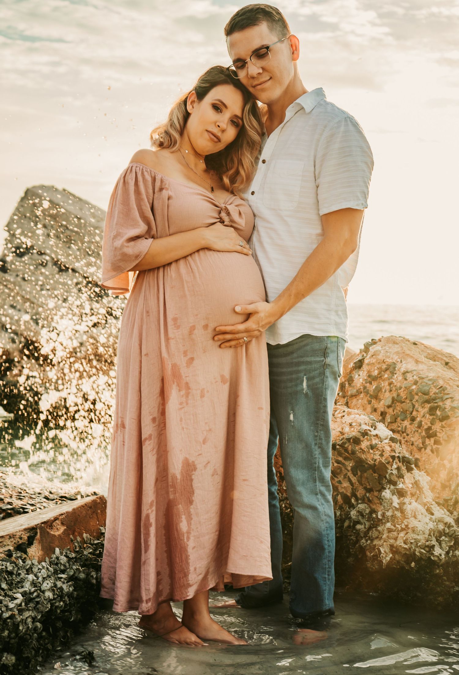 Outdoor Maternity Session at Ft. Desoto in St. Pete, FL; couple embracing near rocks in ocean