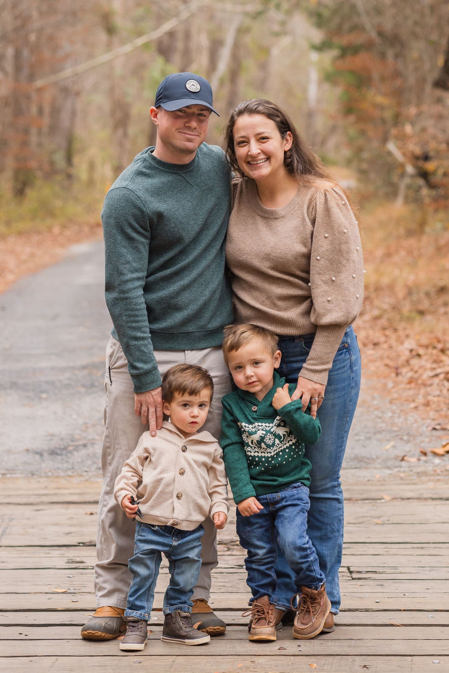 Family of four standing together on wooden boardwalk surrounded by fall foliage.
