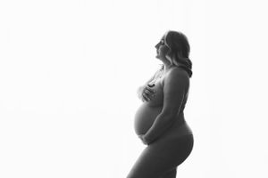 Silhouette of pregnant figure in profile against light background.
