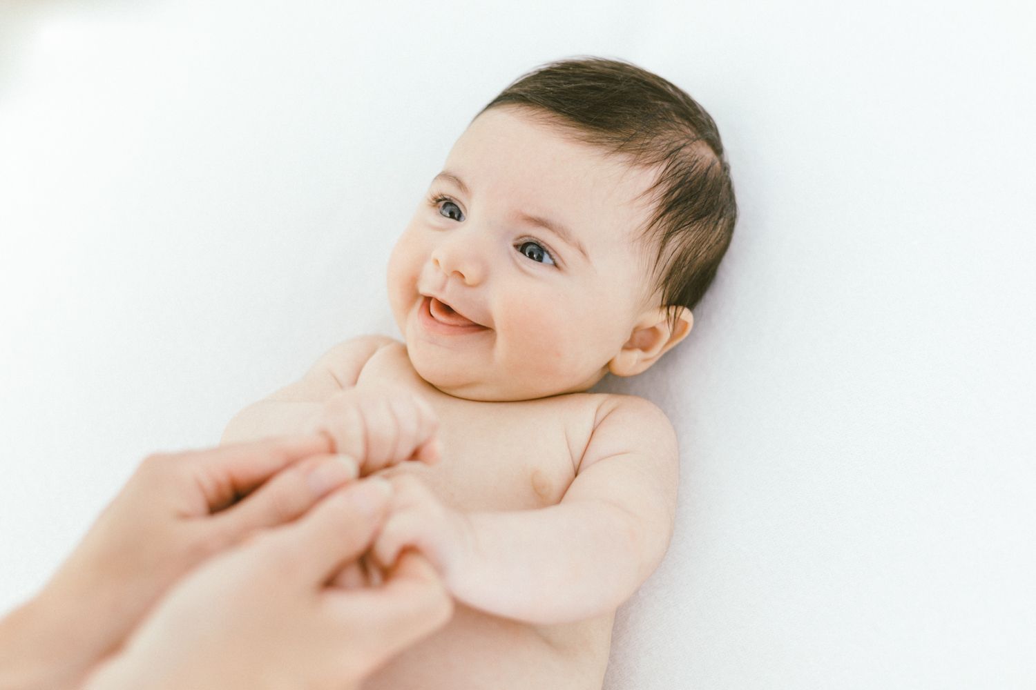Happy baby on white background reaching for hands extended from off-camera.
