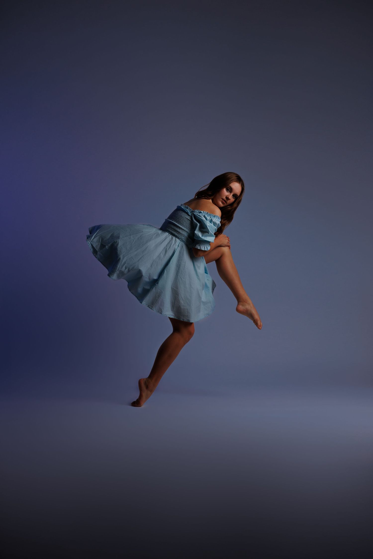 Dancer in flowing blue dress performs graceful aerial pose against dark background.